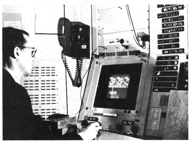 Figure 1. TX-2 operating area &ndash; Sketchpad in use. On the display can be seen part of a bridge similar to those of Figure 15. The Author is holding the light pen. The push buttons &ldquo;draw,&rdquo; &ldquo;move,&rdquo; etc., are on the box in front of the Author. Part of the bank of toggle switches can be seen behind the Author. The size and position of the part of the total picture seen on the display are controlled by the four black knobs just above the tables.